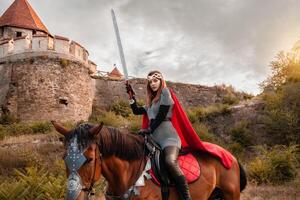 hermosa princesa con rojo capa y con un espada montando un caballo en contra el fondo de un torre y un Roca pared foto