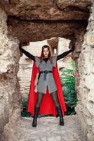 Beautiful Princess with Red Cape and a golden tiara against the stone wall of the tower. photo