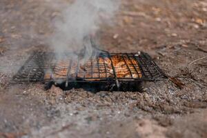 Marinated pork on a grill in the woods. Meat is fried on coals, fire, on the river bank. Grill on the campaign trail. Meat is cooked on charcoal from branches photo
