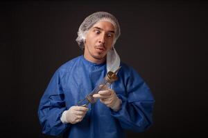 un masculino médico con un terrible antiguo jeringuilla en su manos. el médico en un médico mascarilla, sombrero, túnica y guantes. un horrible. el médico asusta con un enorme jeringuilla con un grueso aguja. foto