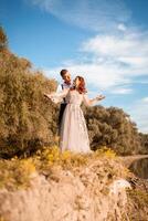 A young wedding couple in love on the edge of a cliff against the backdrop of the river and the sky. A woman in a beautiful gray dress, a man in a suit on the shore of the lake. photo