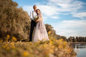 A young wedding couple in love on the edge of a cliff against the backdrop of the river and the sky. A woman in a beautiful gray dress, a man in a suit on the shore of the lake. photo