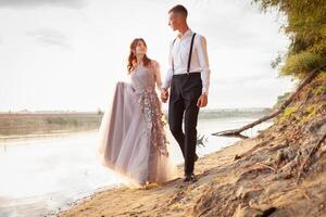 A young wedding couple walks along the river bank, look at each other photo