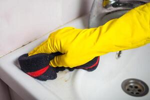 Maid with rubber glove cleaning tap and sink. photo