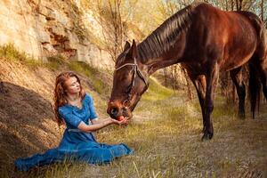 Beautiful girl in a blue dress feeds a horse with an apple photo