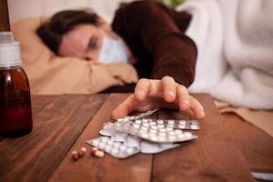 A sick man in a mask against a background of pills and medicines. The man is being treated at home in quarantine. Coronavirus, covid, cold, flu. A man fell ill in a home photo