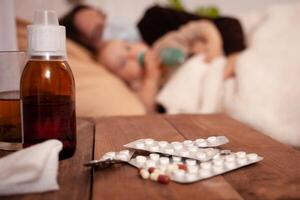 Dad and daughter get sick on the bed against the background of pills and medicines. A man wearing a mask at home. Home quarantine, coronavirus, cold, flu photo