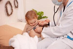 The doctor listens to the heart and lungs of a little girl. Sick baby, home quarantine, coronavirus, covid. photo