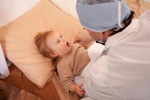 The doctor checks the throat of a little girl at home. Sick baby, home quarantine, coronavirus photo