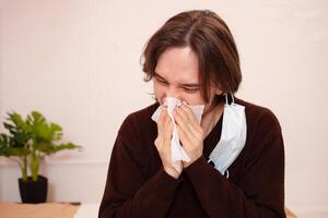 A man sneezes, a medical mask. Empty space for text on a white background. A sick man in home quarantine. Coronavirus photo