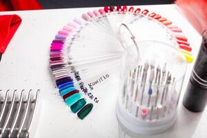 The manicurist holds hands of the client in beauty salon on desktop for manicure with nail polishes, napkins, creams and lighting instruments photo