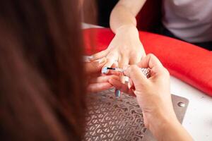 The manicurist holds hands of the client in beauty salon on desktop for manicure with nail polishes, napkins, creams and lighting instruments photo