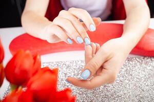 The manicurist holds hands of the client in beauty salon on desktop for manicure with nail polishes, napkins, creams and lighting instruments photo