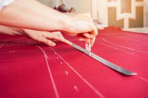 costurera a trabajar. modista haciendo ropa en moderno estudio. Sastre participación lápiz y calificación tela. mujer en pie a mesa con cortar textil, de coser máquina, hilo, patas, agujas, cinta, recortes foto