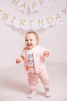 A little girl in a pink suit on a white background celebrates her birthday photo