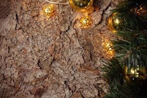 A wooden brown Christmas background with a spruce branch, garland, yellow and gold balls. Empty space for text. Happy New Year. The background is made of spruce bark. photo