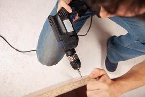 A man drills a hole in the cupboard. A Euro-shunup, screw-screed for a wood chip slab. photo