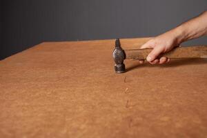 A man hammers nails into a cupboard. The back wall of the cupboard is made of thick cardboard. photo