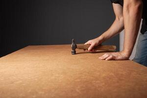 A man hammers nails into a cupboard. The back wall of the cupboard is made of thick cardboard. photo