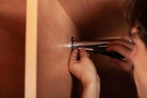 A man twists a pipe for a hanger in a closet with a screwdriver. to hang clothes. photo