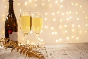 glasses of champagne on a wooden table. The background with a blurred golden garland, sideways. Christmas decorations, background for postcards and congratulations on the New Year. photo