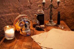 Photo zone in the studio for Halloween. Dramatic scenery for All Saints Day celebrations. The skull is decorated with beads and stones, candles, ink, crow's skull, old parchment on atable.