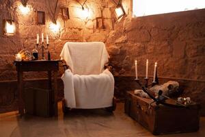 Photo zone in the studio for Halloween. Dramatic intimidating, scenery for All Saints Day celebrations. October 31, photo studio. Armchair, skulls, candles, office, crossbow