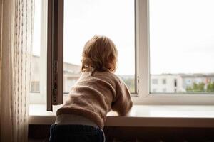 The child climbs to the window, the girl on the window sill rests on the net, the danger of falling. The child is alone at home, can fall out of the window. photo