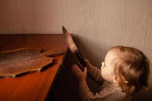 el niño tira un cuchillo desde el mesa. el niño lata cortar, para niños hogar peligros un pequeño un año de edad niña con un cuchillo. foto