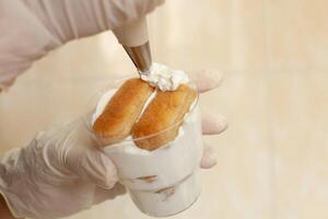 The pastry chef decorates the tiramisu in a glass with whipped cream. photo