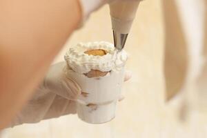 The pastry chef decorates the tiramisu in a glass with whipped cream. photo