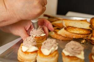 Baskets of puff pastry with butter and pate. Baking on a tray, black. A woman decorates baking with a rose of pate. photo