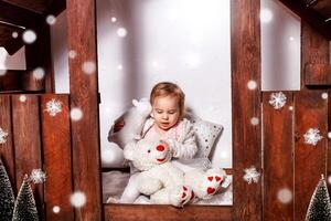 A little girl with toys in a wooden house. Photo studio with Christmas decorations. A happy child plays with toys, white snow, art photography