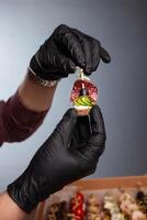 Canape, hands in black gloves hold a beautiful canape on a cap. Catering, snacking, food. Studio photo. photo