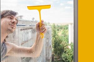 A man washes a window from the outside. The man sprays a blue cleaner photo