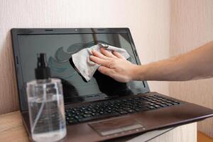 The woman cleans the laptop from dust and bacteria with alcohol spray photo