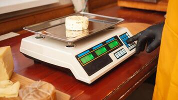 cheesemaker weighs cheese on scales, home production, business. shop photo