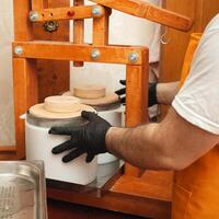 cheesemaker puts cheese under press, whey. Home production, business, portrait. Wooden equipment. photo