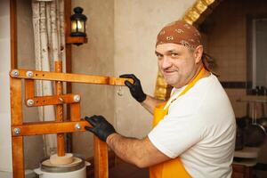 cheesemaker puts cheese under press, whey. Home production, business, portrait. Wooden equipment. man smiling, portrait photo