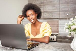 Portrait of beautiful African American freelancer woman, table in kitchen. Work on laptop, indoor. Smiling photo