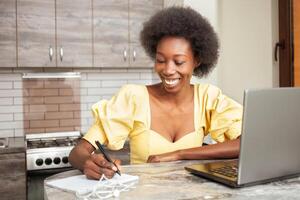 Portrait of beautiful African American freelancer woman, table in kitchen. Work on laptop, indoor. work from home photo