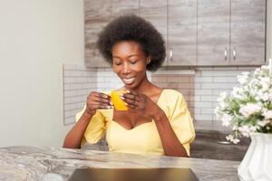 beautiful African American woman drinks tea in kitchen. Enjoying drink, hot coffee in morning, breakfast. charge of energy and vivacity for whole day. Smiling photo