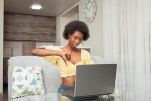 portrait African American black woman at home. Indoor, woman is frightened, shocked, unpleasantly surprised, angry. Emotions, sitting in front of laptop. dislike, thumb down photo