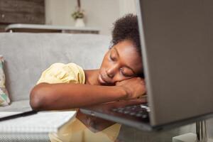 African American black woman freelancer sleeps in workplace near laptop, working at home, tired. deadline photo