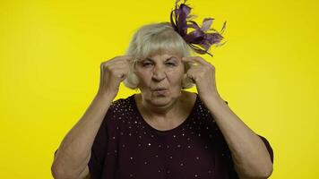 Displeased annoyed senior old woman showing stupid gesture. Elderly grandma on yellow background video