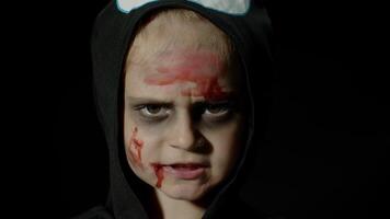 Halloween, en colère fille avec du sang maquillage sur affronter. enfant habillé comme effrayant squelette, poser, fabrication visages video