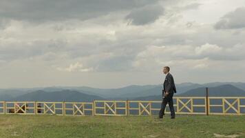 Groom, brunette young man walking on the top of the mountains. Slow motion video