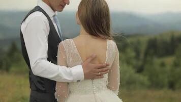 The groom strokes the bride's back near mountain hills. Wedding couple video