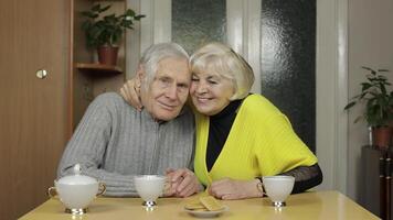 Happy old grandparents couple sit on table at home enjoy drinking tea together video