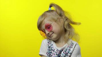 Child smiling, looking at camera. Girl tourist in pink sunglasses posing on yellow background video